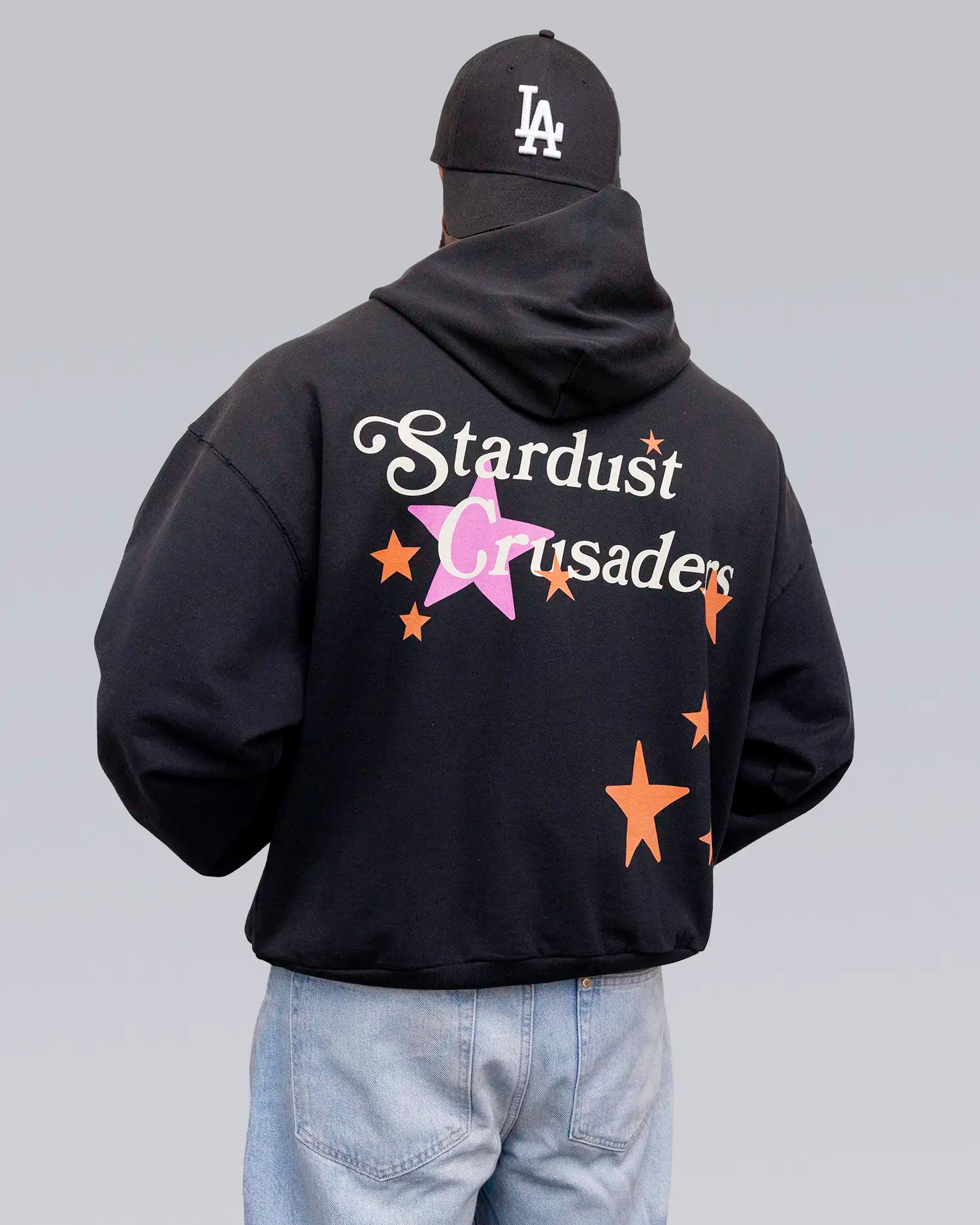 Person wearing a black hoodie with 'Stardust Crusaders' text and star graphics, standing against a gray background. option1_black