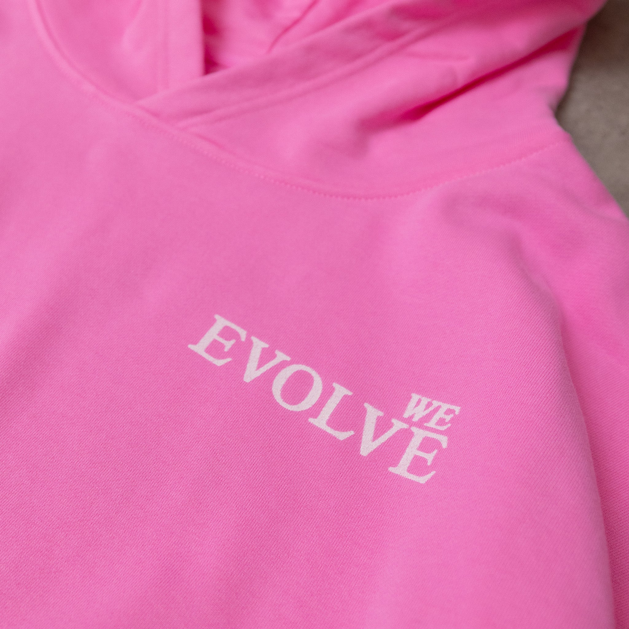 Pink hoodie with 'EVOLVE WE' text on a plain background