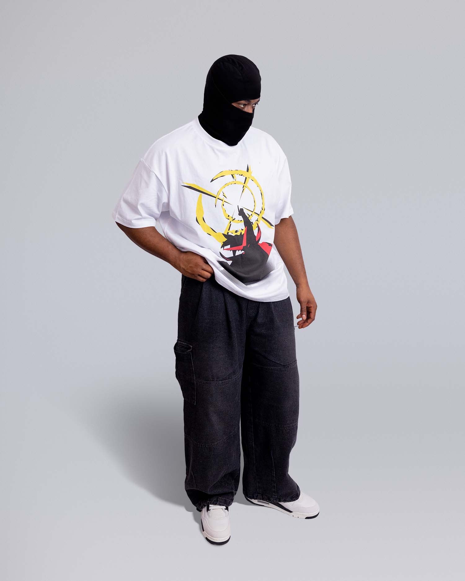 Person wearing a white t-shirt with a graphic design, black pants, and a black balaclava on a light gray background