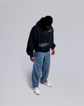 Person wearing a black hoodie and blue jeans on a light gray background