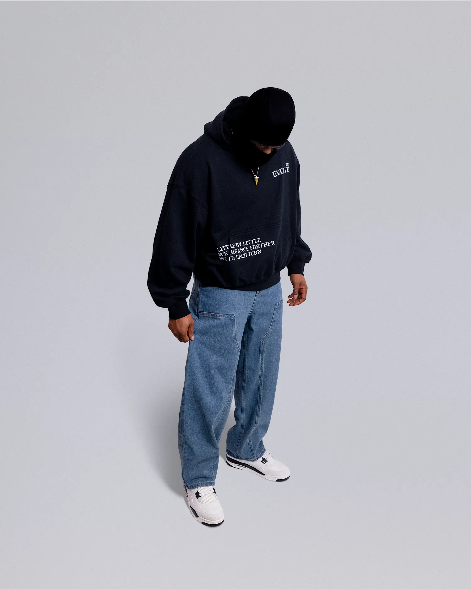 Person wearing a black hoodie and blue jeans on a light gray background