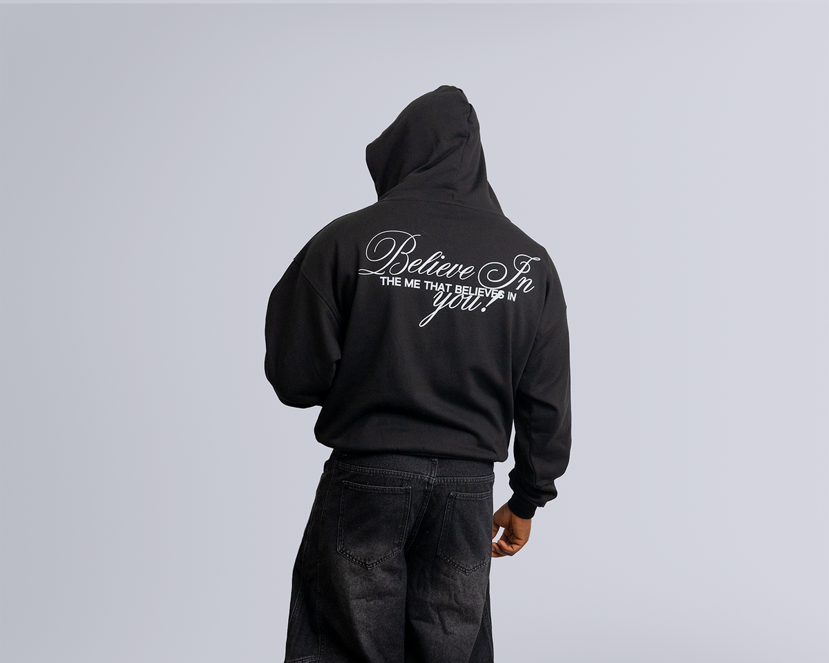 Person wearing a black hoodie and pants with text on the back, standing against a plain background