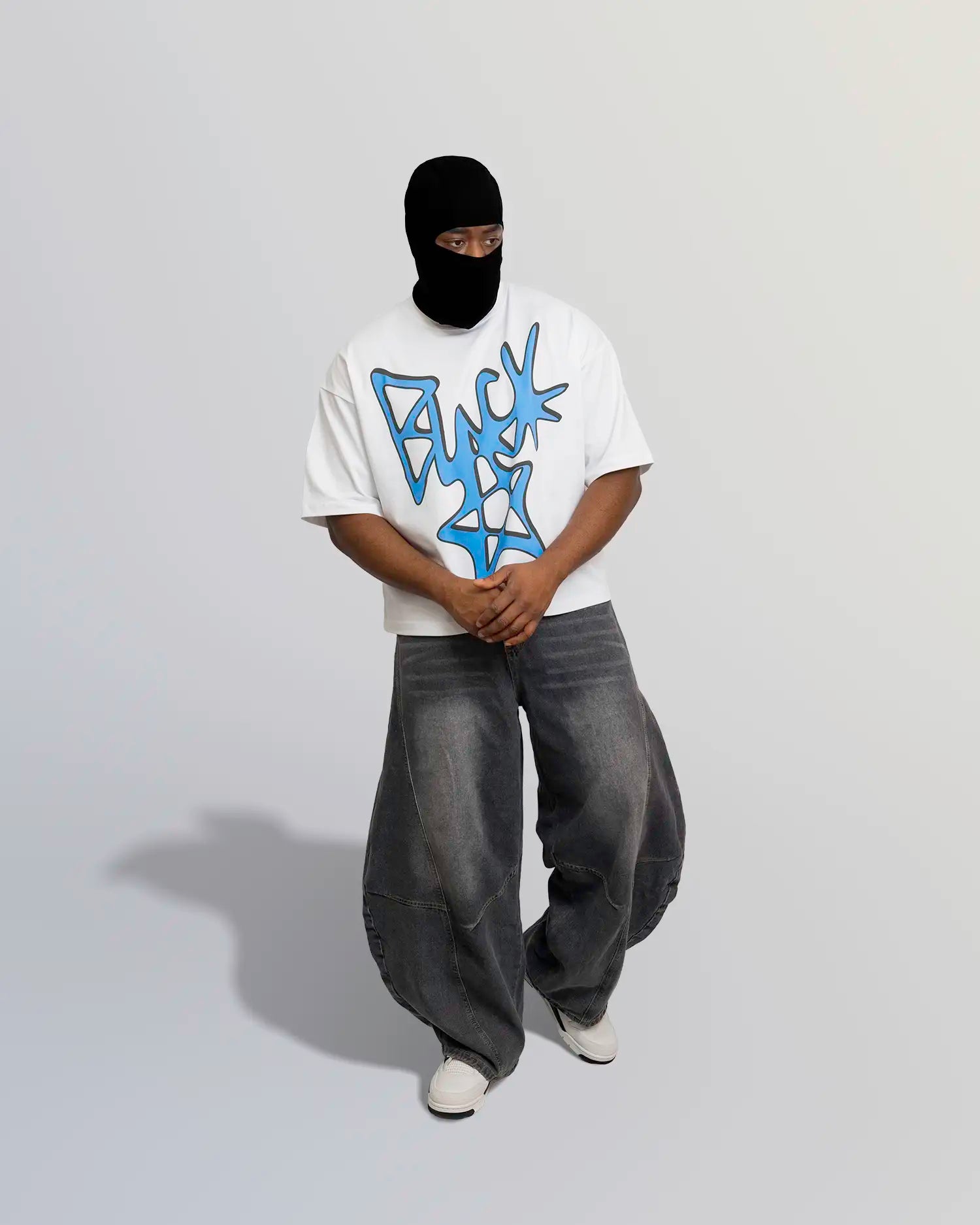 Person wearing a white t-shirt with blue graphic design and dark pants on a plain background option1_white