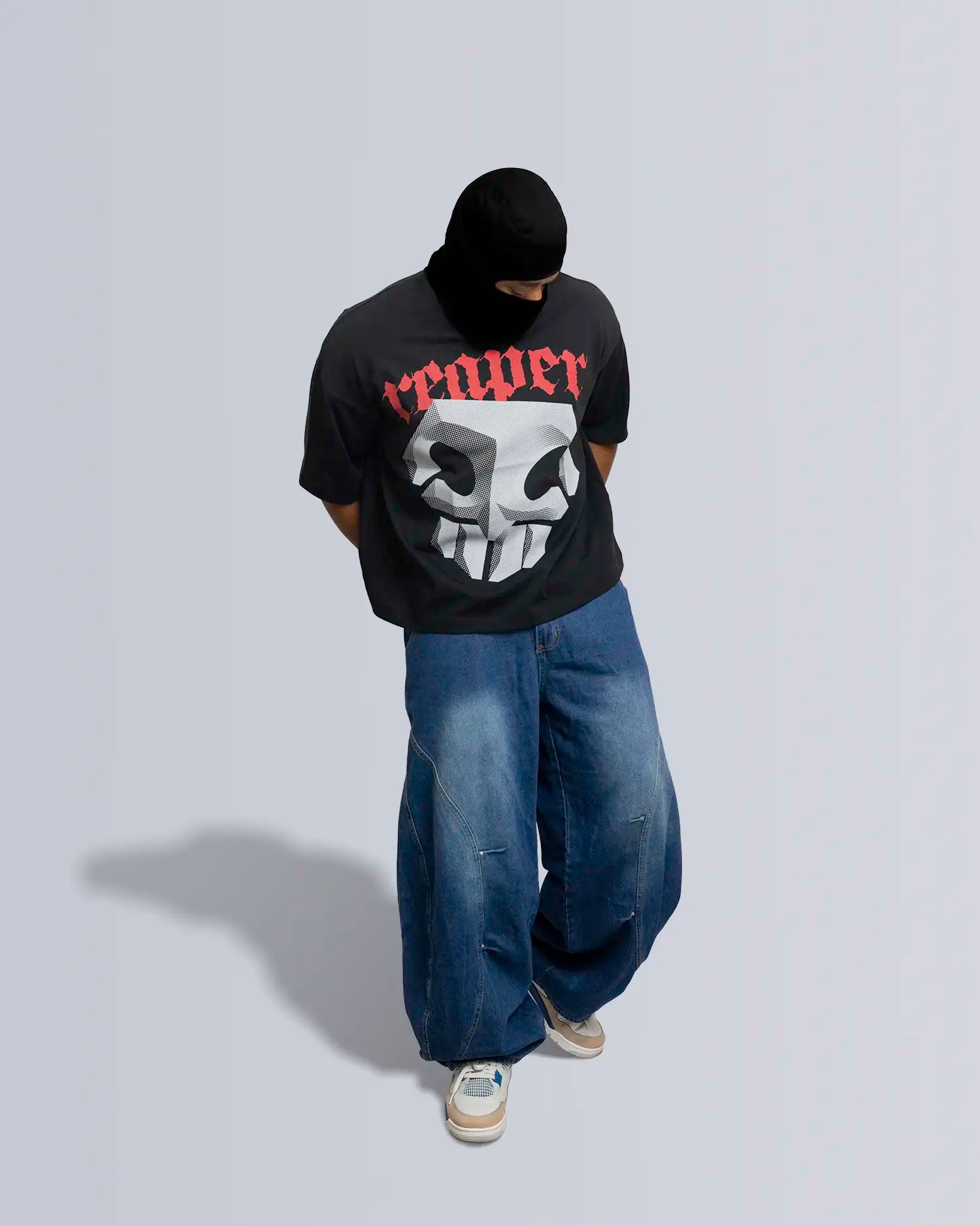 Person wearing a black t-shirt with a graphic design and text, blue jeans, and white sneakers on a light gray background option1_black